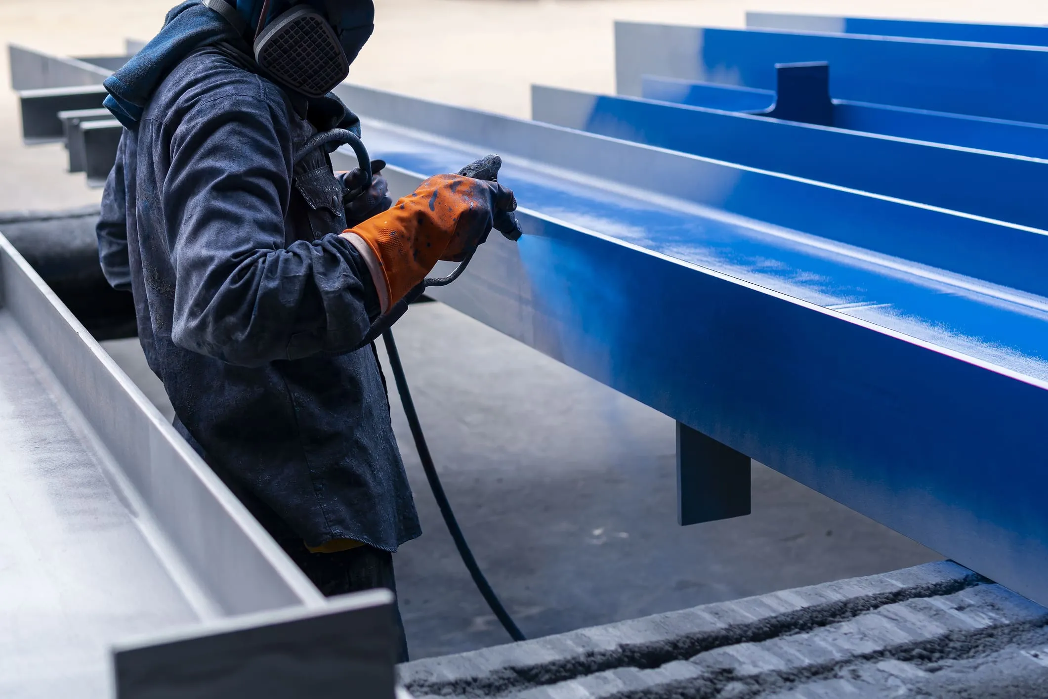 Technician applying a protective coating to a row of structural steel beams in the shop