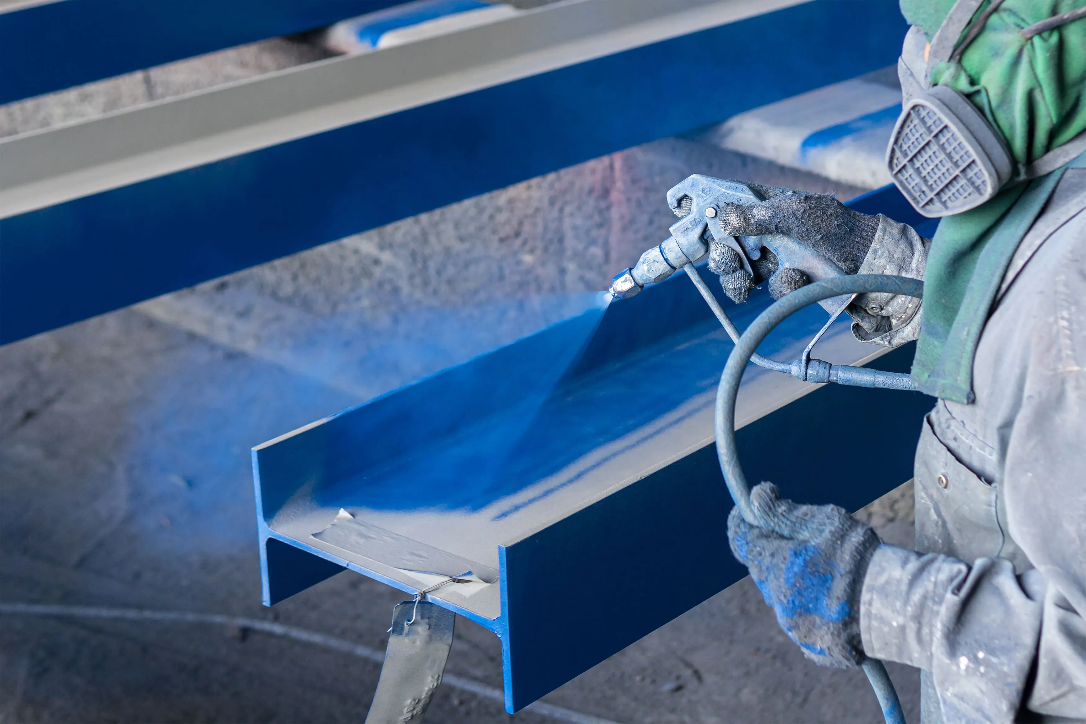 High-performance blue protective coating being sprayed onto a structural steel beam